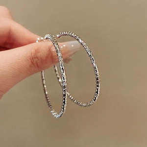 Close-up of silver hoop earrings with textured spiral design and metallic glossy finish