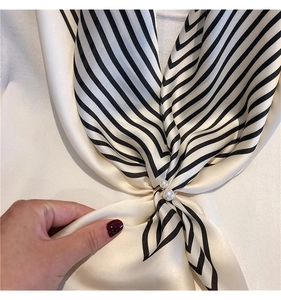 Detail of golden double pearl scarf ring styling a black and white striped silk scarf