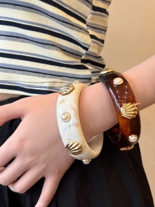 Detail of resin shell and pearl bangle bracelets in amber and ivory marble finish