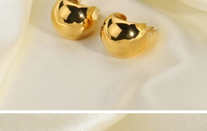 Close-up of chunky gold hoop earrings on beige silk fabric with reflective finish