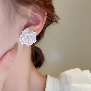 Close-up of white 3D flower stud earrings with matte petals on a female model