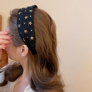 Détail du serre-tête en tissu noir orné d'étoiles métalliques dorées porté par un mannequin