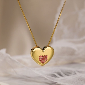Detail shot of a golden heart pendant necklace with red cubic zirconia on lace background
