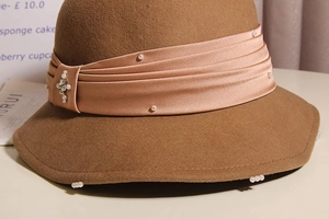 Close-up of wool cloche hat with silk ribbon, white pearls and sparkling rhinestones