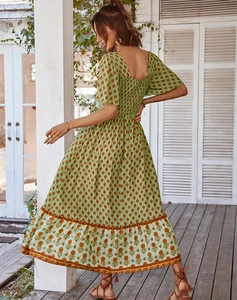 Detail of green floral dress featuring a square neck and ruffled hem in an outdoor setting