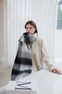 Detail of elegant black and white plaid knit scarf with fringes worn by a model indoors