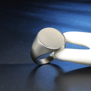 Macro detail of silver brushed stainless steel signet ring held by a white model hand