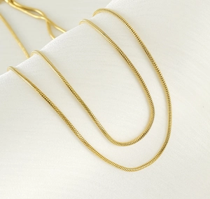 Detailaufnahme der zweilagigen 18K vergoldeten Schlangenkette auf weißer Seide