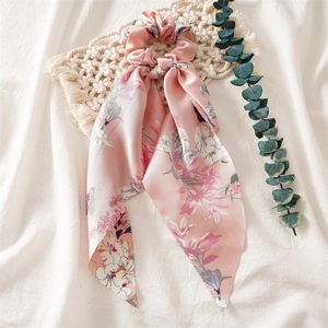Pink floral satin scrunchie with streamer on a minimalist woven mat background