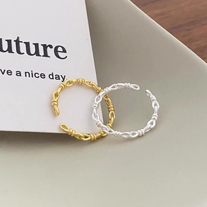 Detail showing gold and silver braided chain knot rings on a minimal ceramic tray