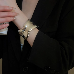 Close-up of irregular wide gold cuff bracelet featuring a minimalist wavy metal texture