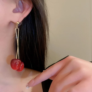 Close-up of red cherry drop earrings with gold chains worn by a model in soft light