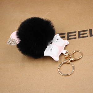 Close-up of black faux fur pom-pom keychain with a white fox head and golden glitter ears