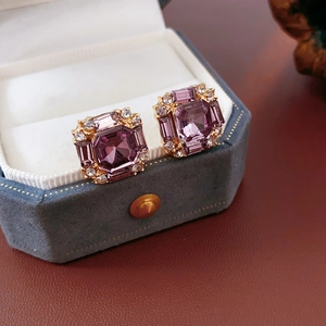 Macro detail of rectangular purple gemstone earrings with diamond halo in a blue velvet box