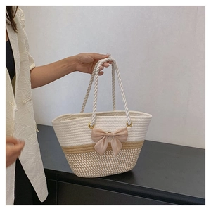 Detail of woven tote bag with two-tone design, beige bow accent, and rope handles