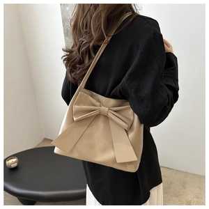 Detailed view of large bow on beige leather tote bag carried by a model