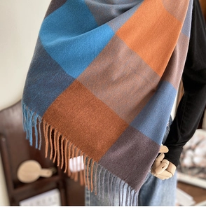 Close-up of thick plaid scarf featuring blue, orange, and brown tassels and woven texture