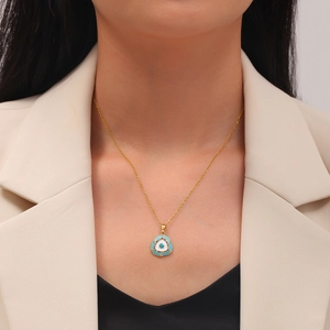 Detail of a triangle Evil Eye pendant on a gold chain worn by a female model