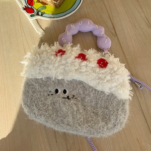 Detail of cute grey cake-shaped plush crossbody bag with purple handle on wooden table