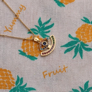 Macro view of evil eye pendant with multicolored zircons on gold beaded chain