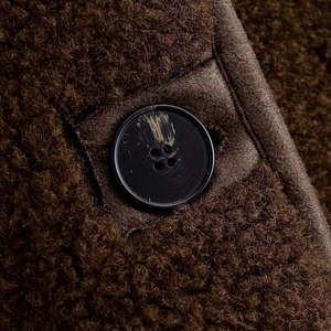 Détail de la veste en fausse fourrure marron foncé avec bouton mat et bordure en cuir