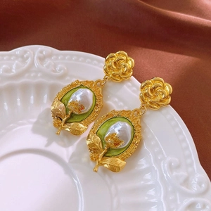 Detail of vintage gold rose earrings with green enamel and white pearl on a ceramic tray