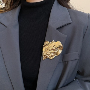 Macro detail of large pleated golden leaf brooch on a dark suit lapel with artistic texture