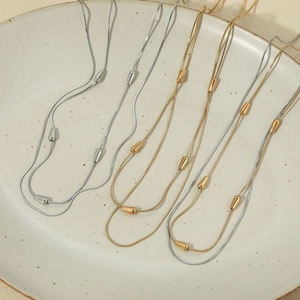 Layered stainless steel snake chain necklace with droplet beads on ceramic tray