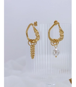 Detail of asymmetric gold tassel and faux pearl earring on a ribbed glass holder