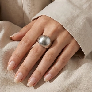 Close-up of polished silver stainless steel dome ring worn on finger over linen