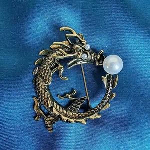 Detailansicht der Vintage-Drachenbrosche aus Bronze mit Perle auf blauem Seidenstoff