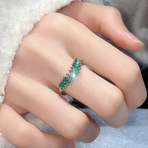 Silver open ring with row of sparkling emerald green zircons on a soft textured background