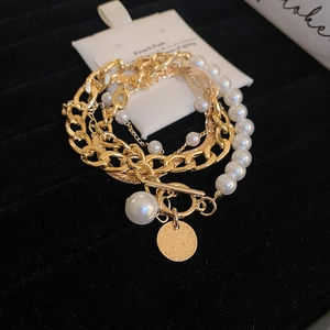 Detailed view of layered gold chain and pearl bracelets with OT toggle and textured pendant