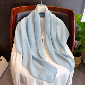 Texture dettagliata di una sciarpa in cotone e lino azzurro drappeggiata su camicia bianca