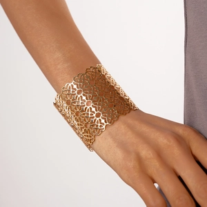 Dettaglio di un bracciale rigido dorato traforato con trama floreale su polso femminile