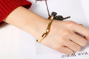 Close-up of a women's gold titanium steel geometric bangle worn with a red sweater