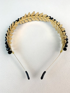 Detail of handmade gold leaf headband with black crystal beads on a white textured surface