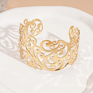 Close-up of golden hollowed floral pattern open cuff bracelet on a white ripple plate
