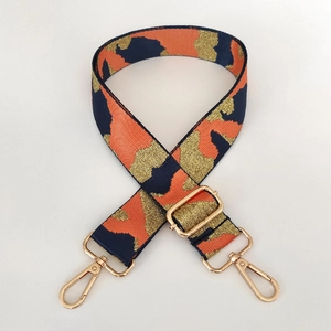 Detail of adjustable camouflage bag strap with orange patterns and gold metal lobster clips