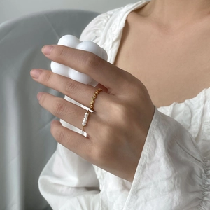 Detail of gold pearl ring set and geometric ring worn against white cloud candle