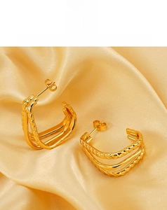 Close-up of golden layered C-shape earrings with braided texture on silk fabric