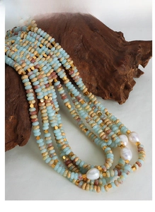 Detail of beaded necklace with light blue stones, brown beads and baroque pearls on wood