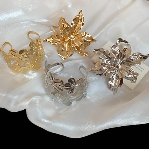 Detailed view of large metallic flower cuff bracelets with hammered texture on white silk
