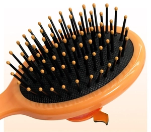 Close-up of pumpkin hair brush with black bristles and orange tips on a cream background
