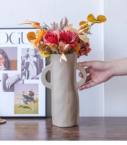 Detail einer minimalistischen unregelmäßigen beigen Keramikvase mit Griffen auf Holztisch
