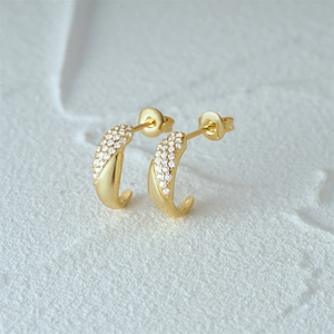 Macro view of 18K gold J-shaped earrings featuring pave-set white crystals and butterfly back