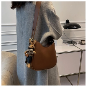 Brown leather shoulder bag with cute plush rabbit charm worn over a grey wool coat
