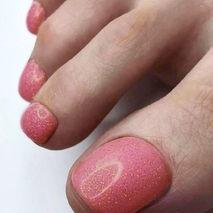 Close-up of pink glittery toenail art featuring golden sparkles and a glossy gel finish