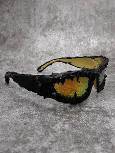 Detailed macro view of black avant-garde sunglasses with orange gradient lenses and lava texture