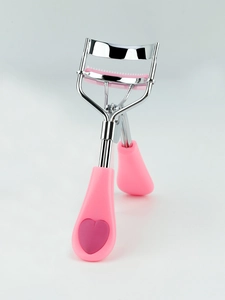Close-up of pink heart-shaped eyelash curler handle with polished steel comb details